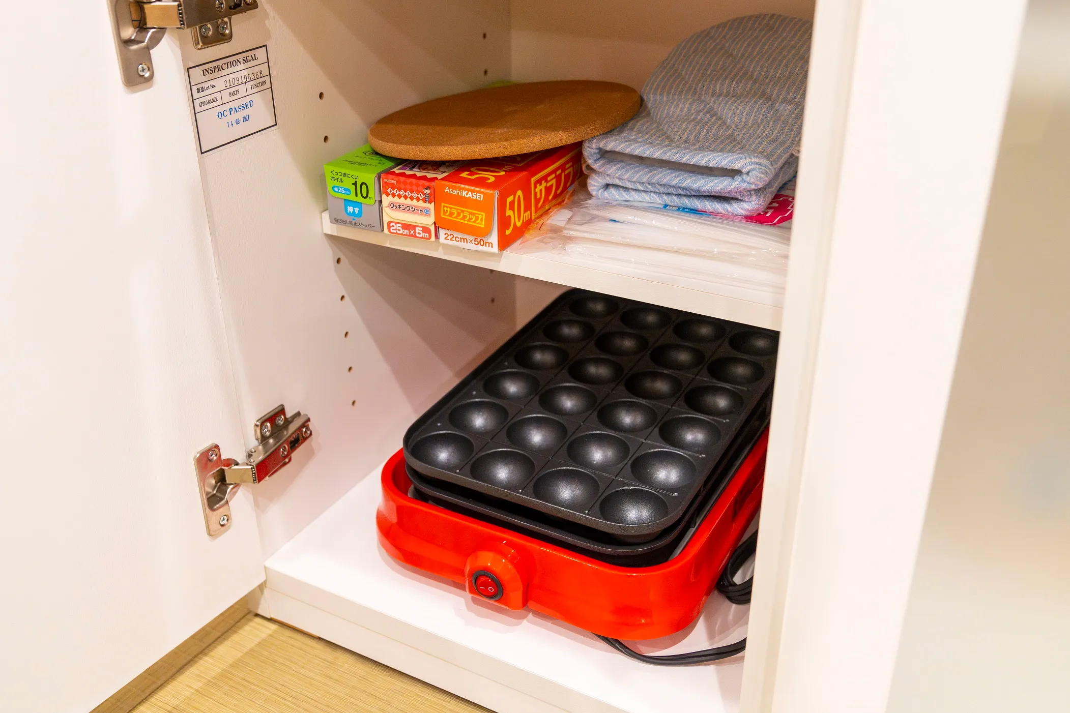 An electric takoyaki pan stored in the kitchen cupboard beside cookware