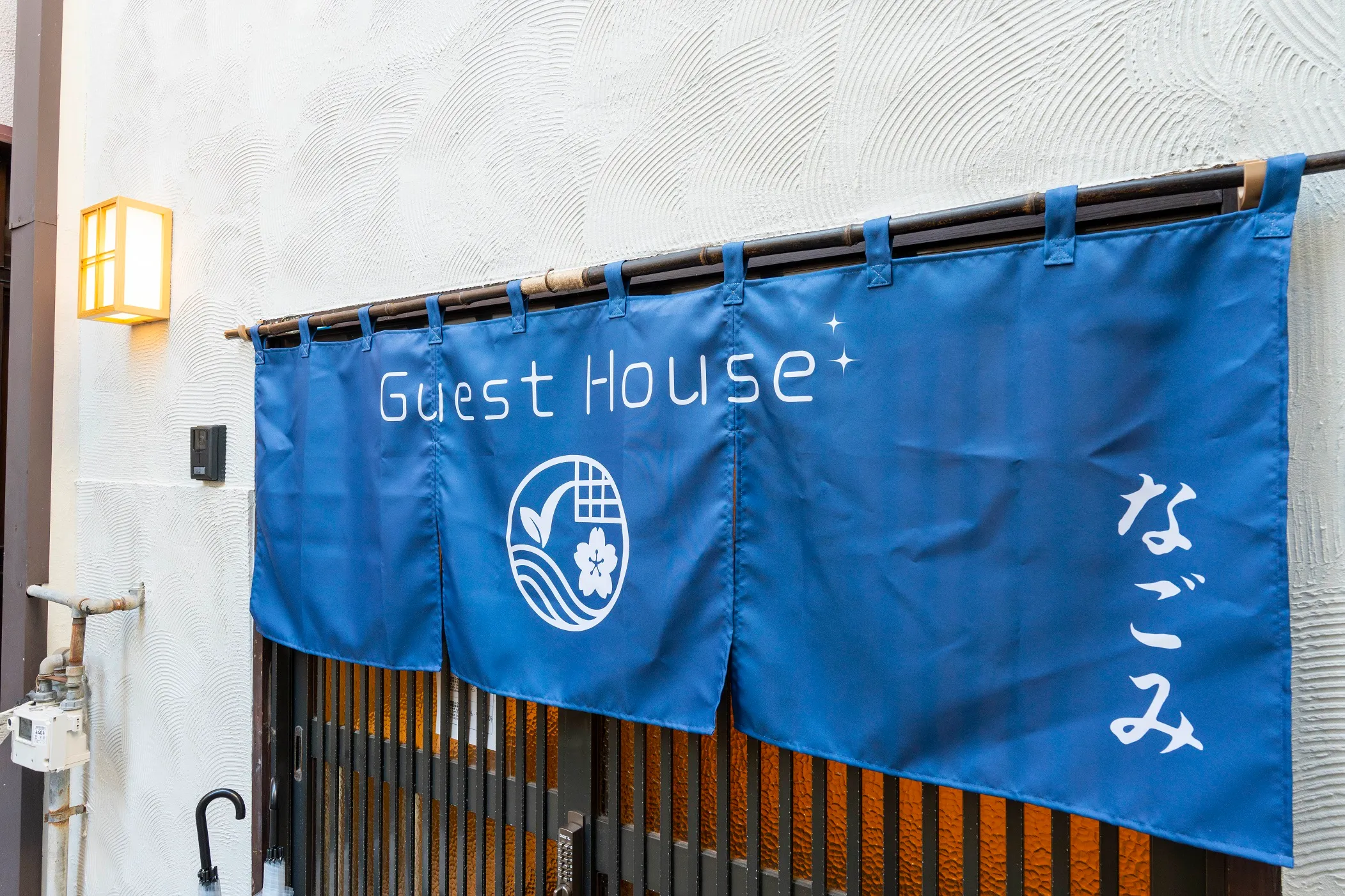 The indigo noren curtain hanging at the entrance to Nagomi Stay Osaka, lettered Guest House なごみ