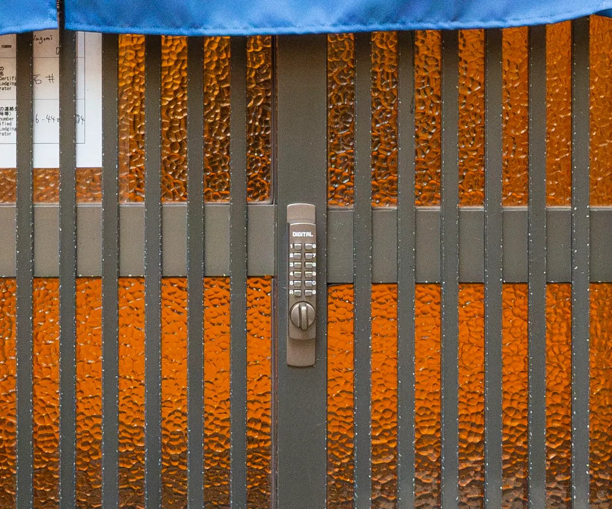 The lattice entrance gate with a keypad lock, amber glass glowing behind it